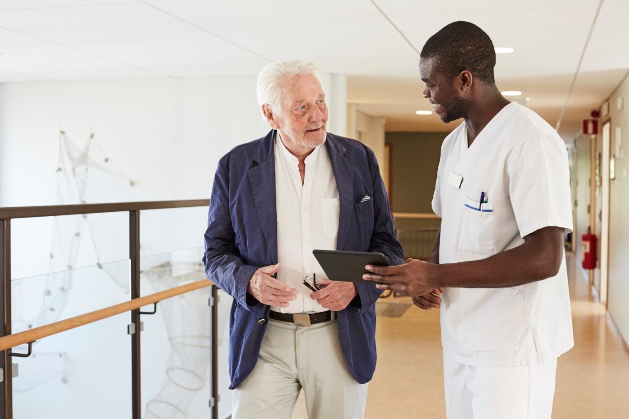 A young medical professional helps his mature patient in finding the best options for him on iPad