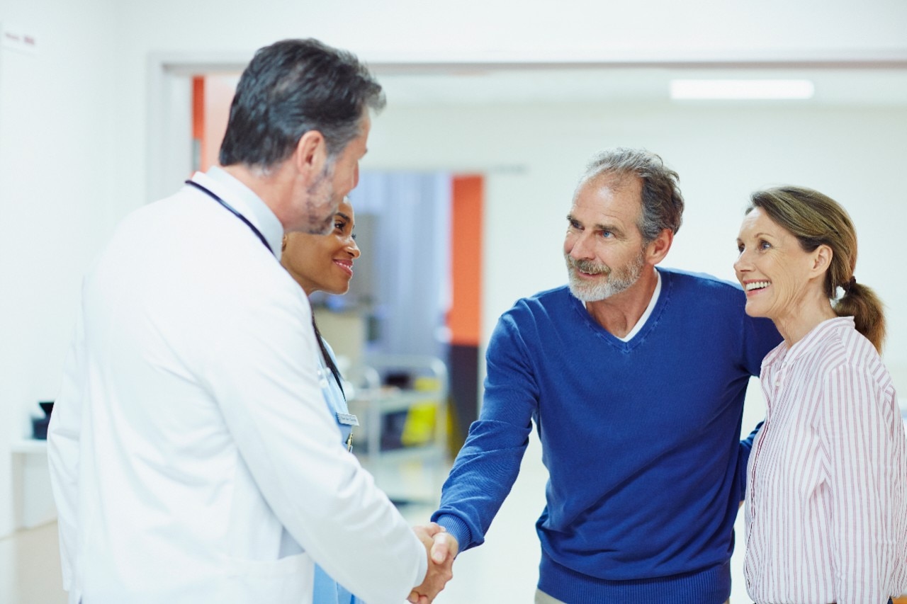 A medical professional shakes hands with his patents in the hallway of the hospital and keeps them updated on what is happening.