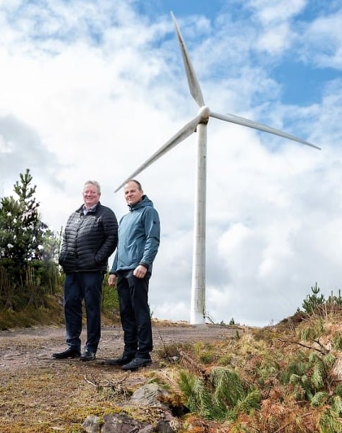 Image of two Medtronic staff standing in front of a wind turbine that supplies power to our Galway plant.