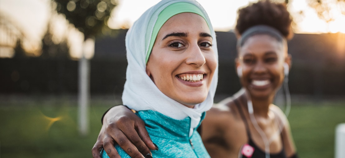 Two women in athletic wear smiling in a park.