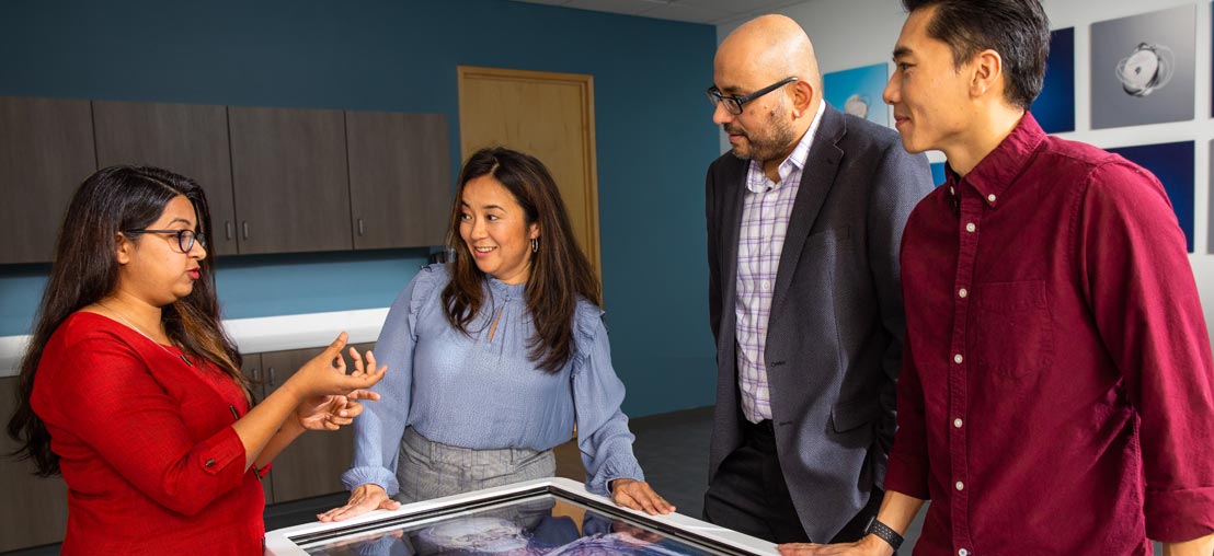 Employees listen to woman explaining something while using a virtual anatomy table.